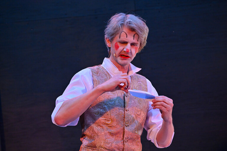 Werther (Thomas Maria Peters) mit Clown Make-Up faltet einen Papierflieger